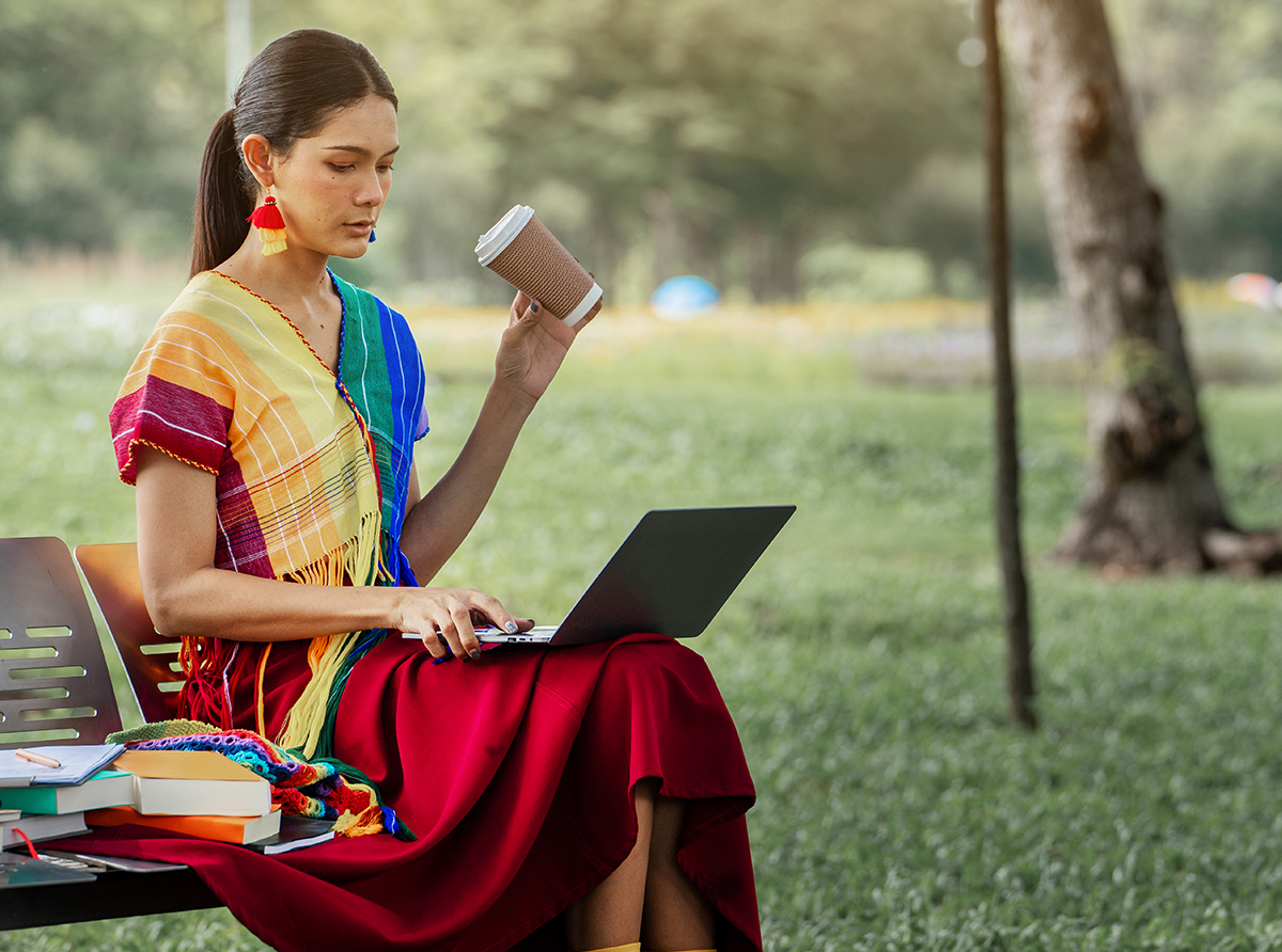 A student sitting in a university campus using a laptop for studies.