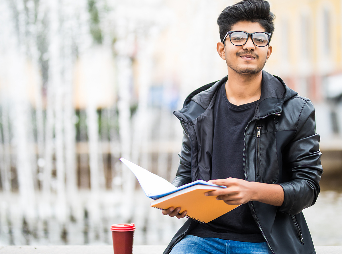 A student looking at the camera while holding a book inside a university.