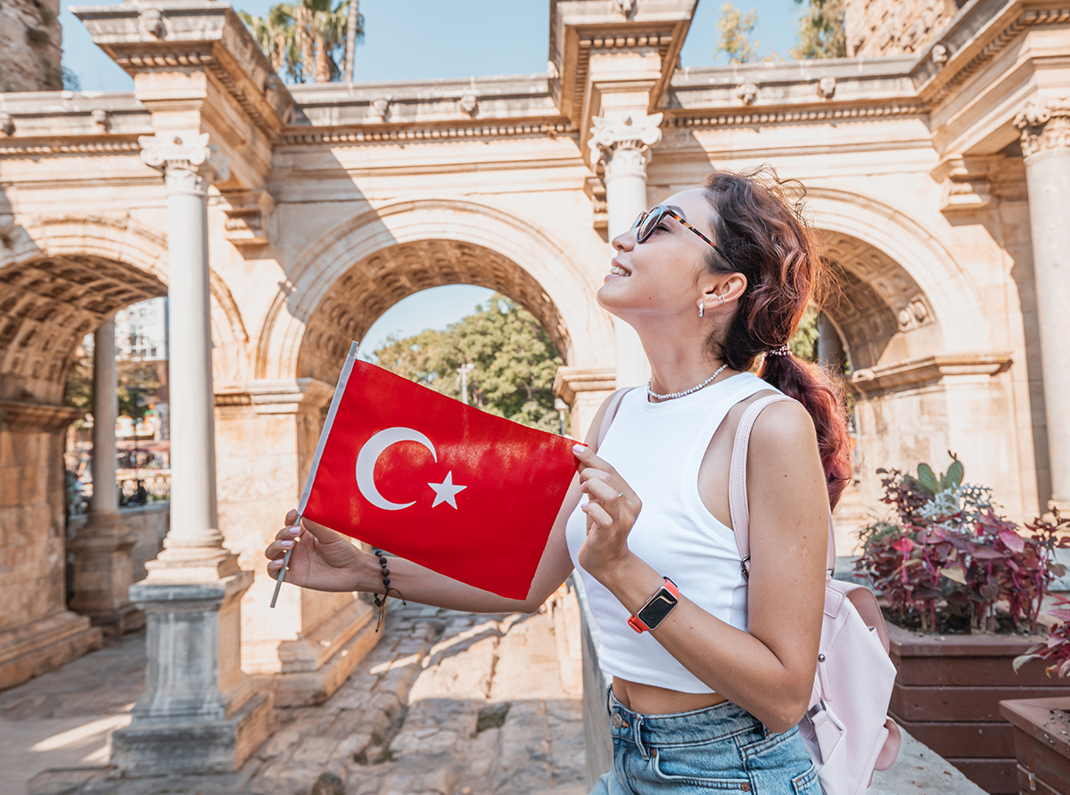 A happy student girl holding the Turkish flag at a historic site, symbolizing academic pride.