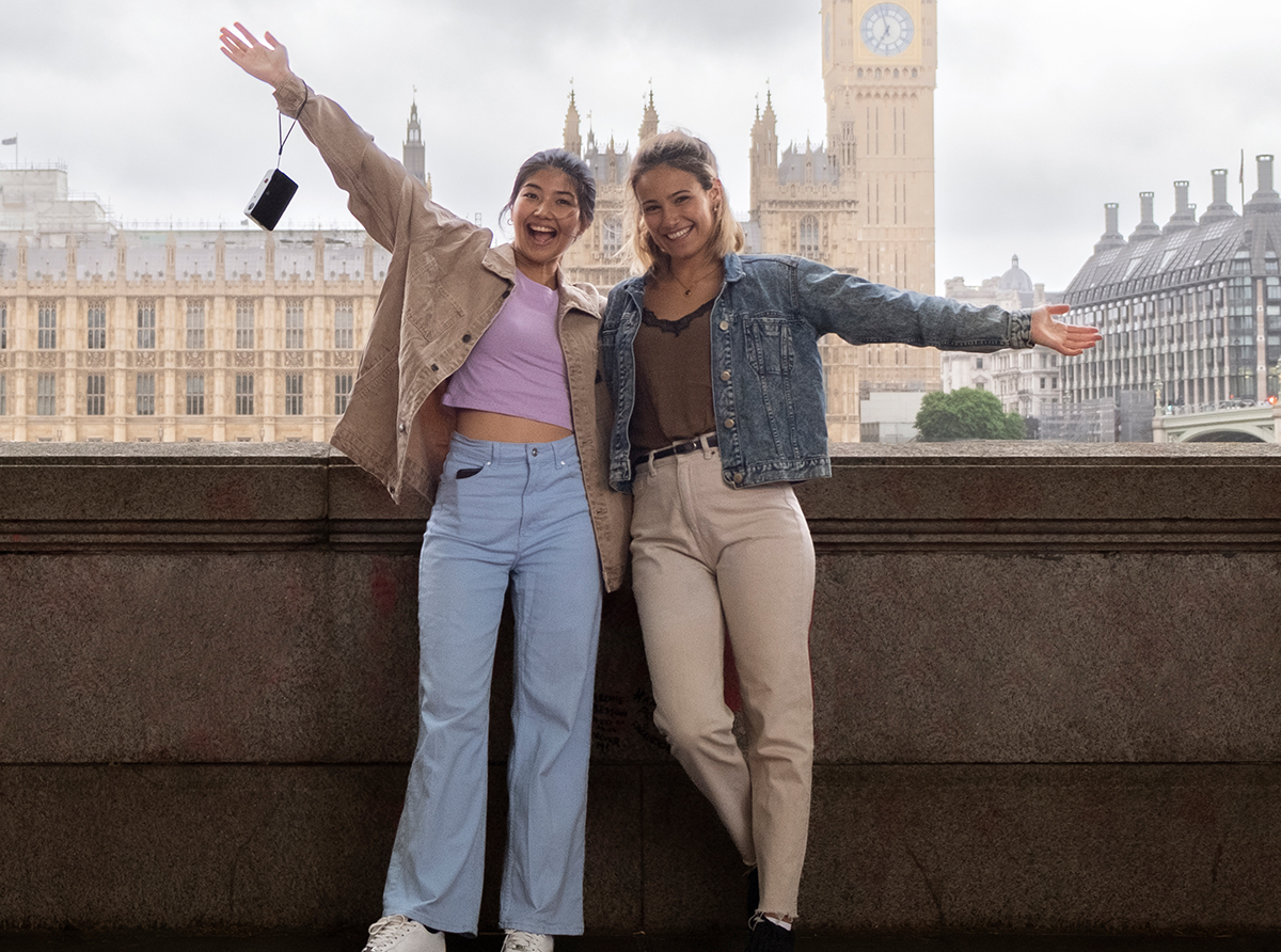 Two student girls standing and waving in front of Big Ben, embracing their study abroad experience.